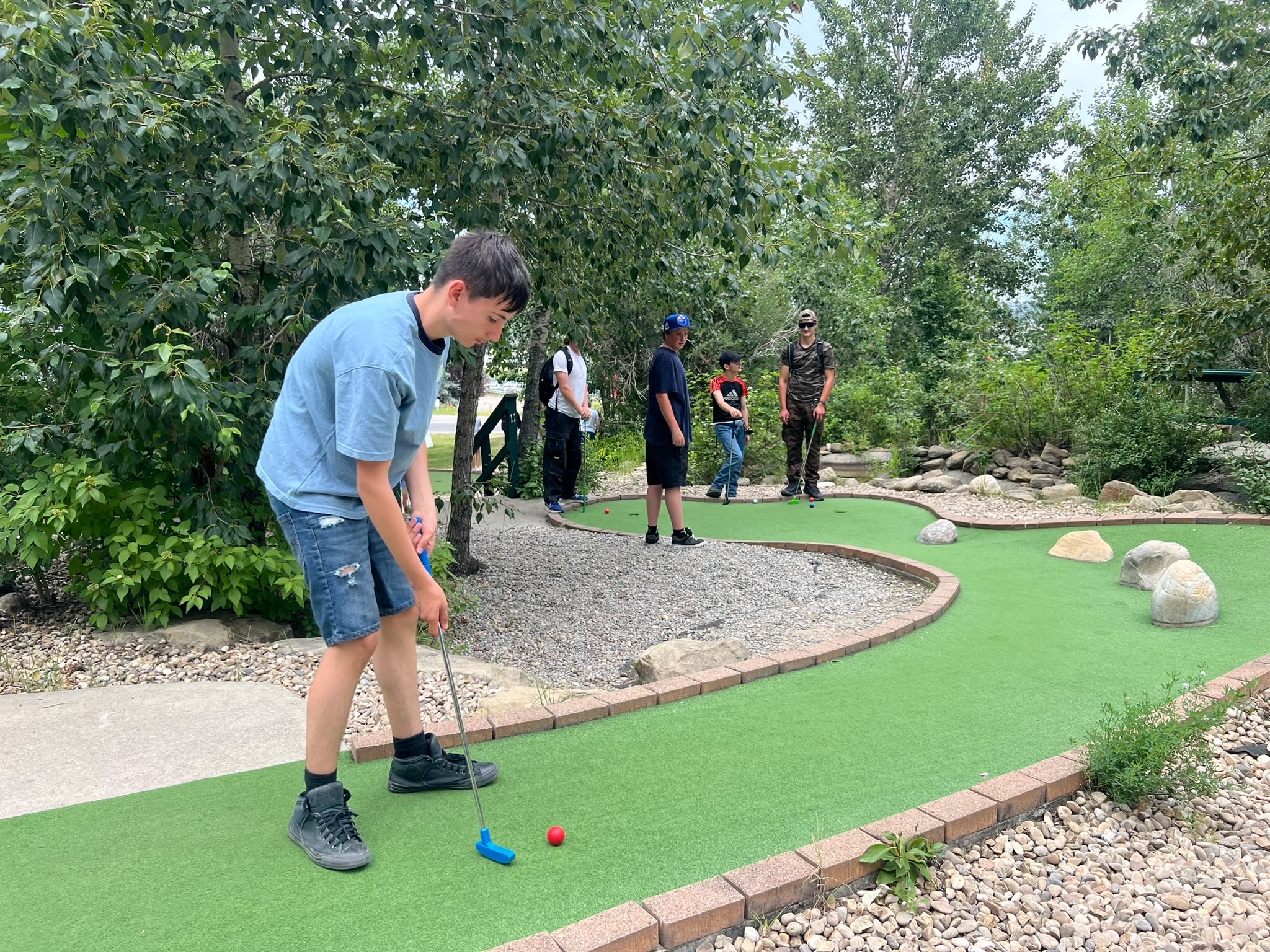 Mini golf A group of campers playing miniature golf together on an outdoor course surrounded by trees.