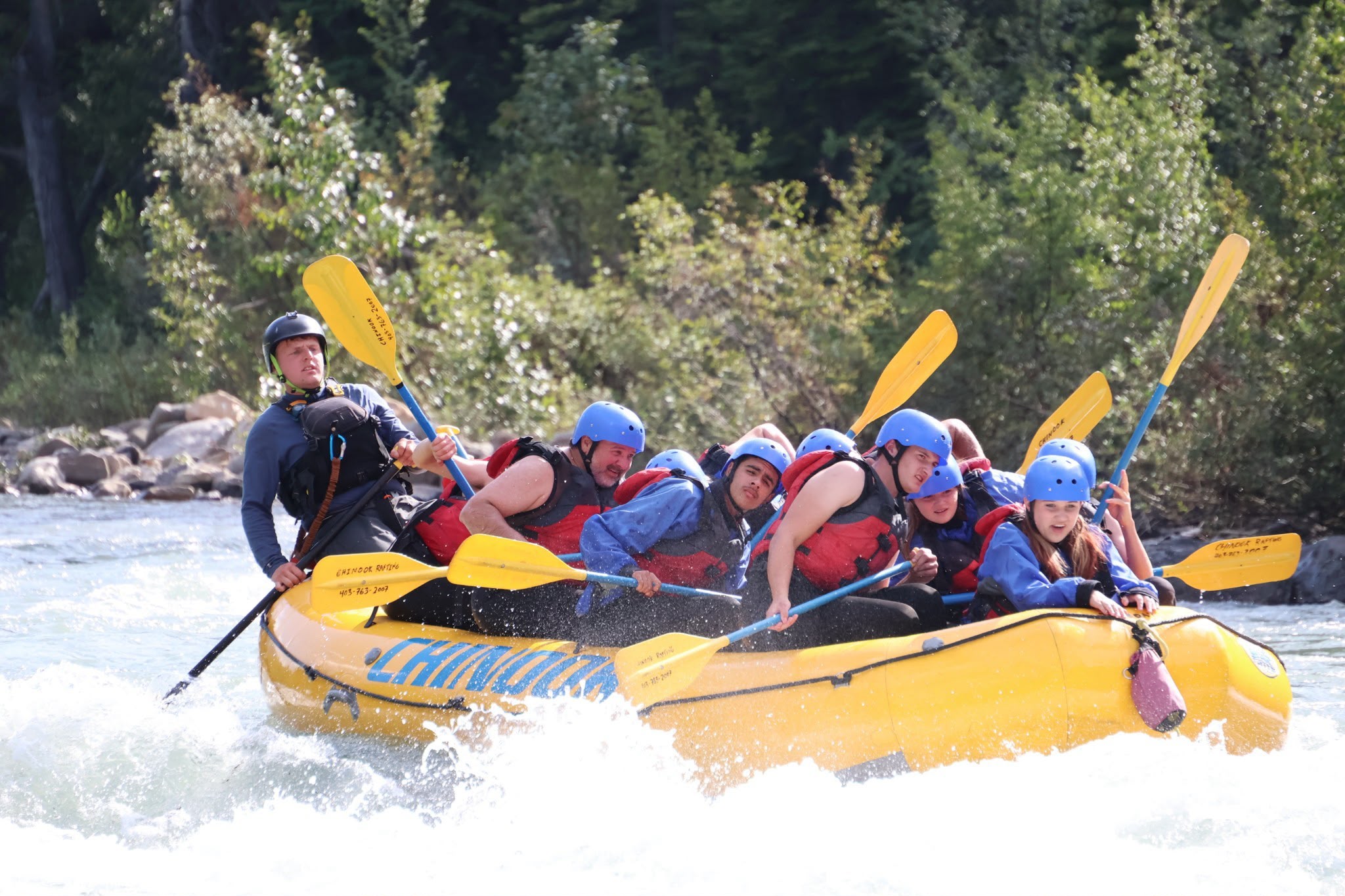 White-water rafting Campers wearing helmets and life jackets paddle together through white-water rapids in a yellow raft.
