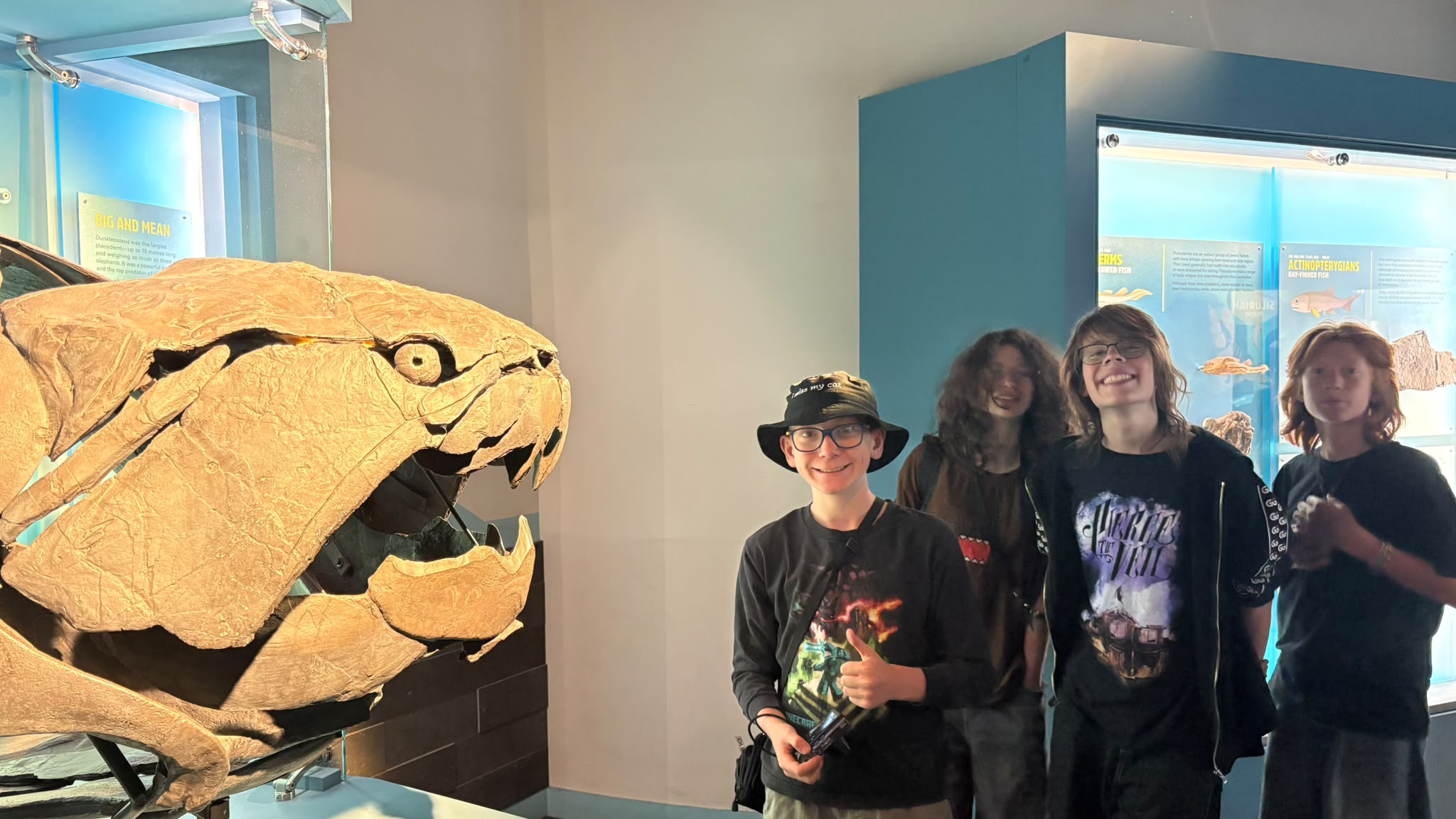 Museum / fossil exhibit Four campers posing beside a large prehistoric fish fossil exhibit during a museum visit.