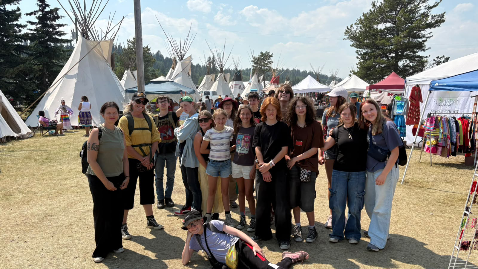 Group with Teepee Campers and staff posing together outdoors among tipis and market tents during a summer camp outing.